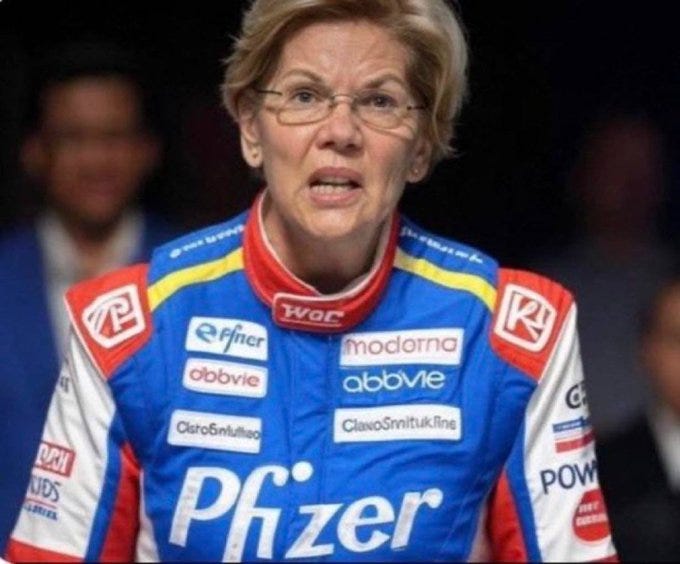 Elizabeth Warren wearing a blue racing suit with red and yellow accents. The suit features logos including Pfizer, AbbVie, Moderna, and GlaxoSmithKline prominently on the front. Elizabeth Warren wearing a blue racing suit with red and yellow accents. The suit features logos including Pfizer, AbbVie, Moderna, and GlaxoSmithKline prominently on the front.