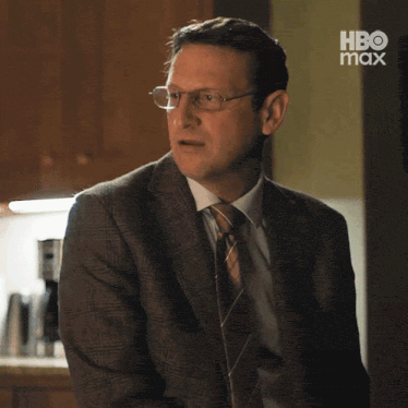 a man in a suit and tie is standing in front of a hbo max sign .