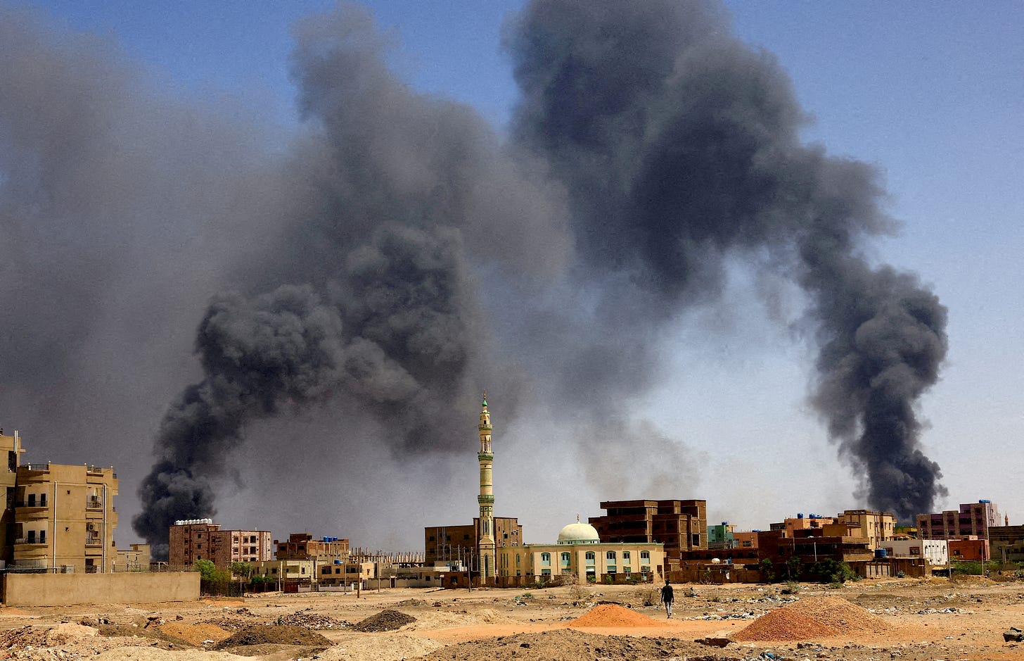 Man walks while smoke rises above buildings after aerial bombardment in Khartoum North Man walks while smoke rises above buildings after aerial bombardment in Khartoum North