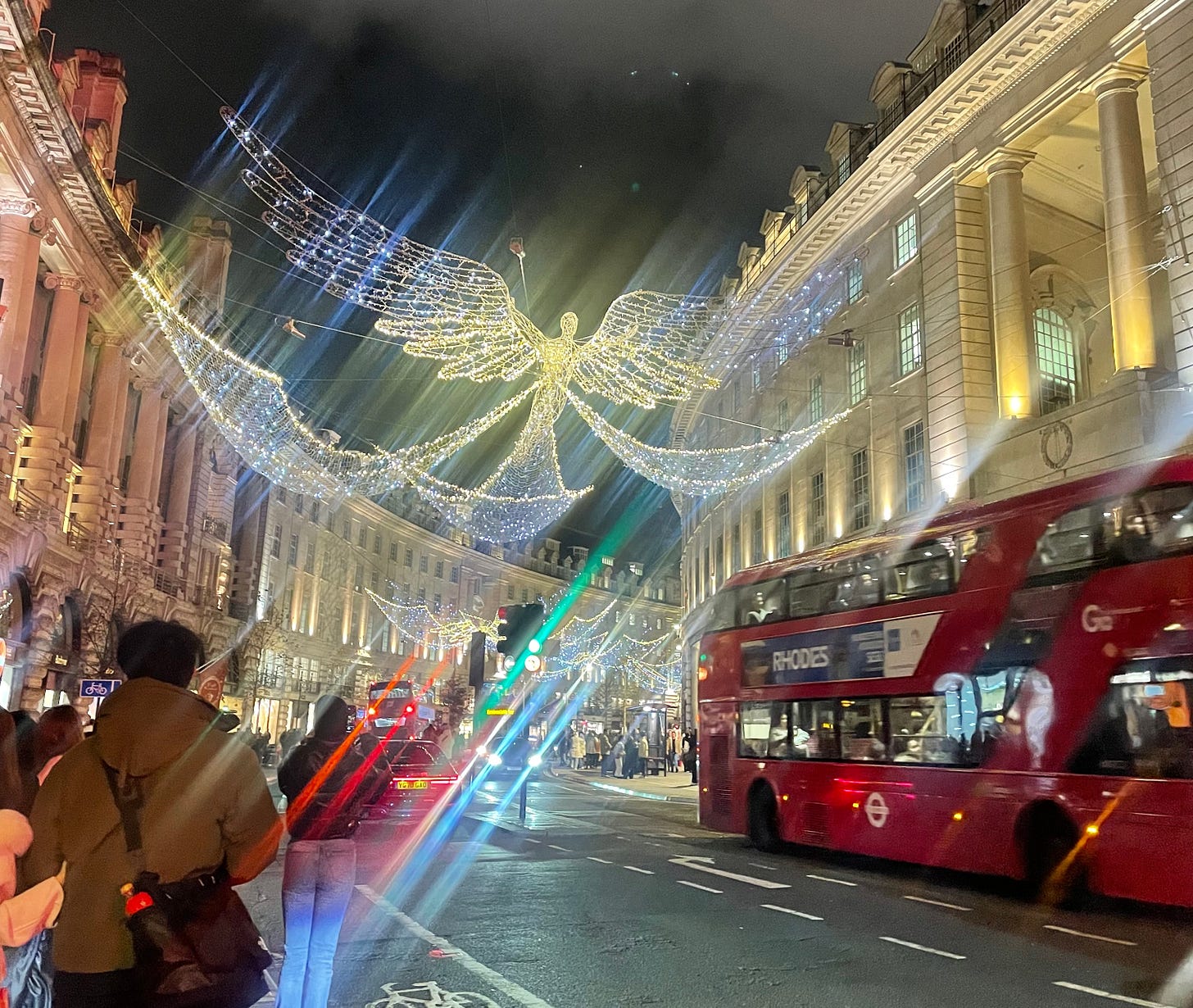 Christmas lights strung over Regents Street at night in the shape of flying angels. There's a red London bus in the foreground