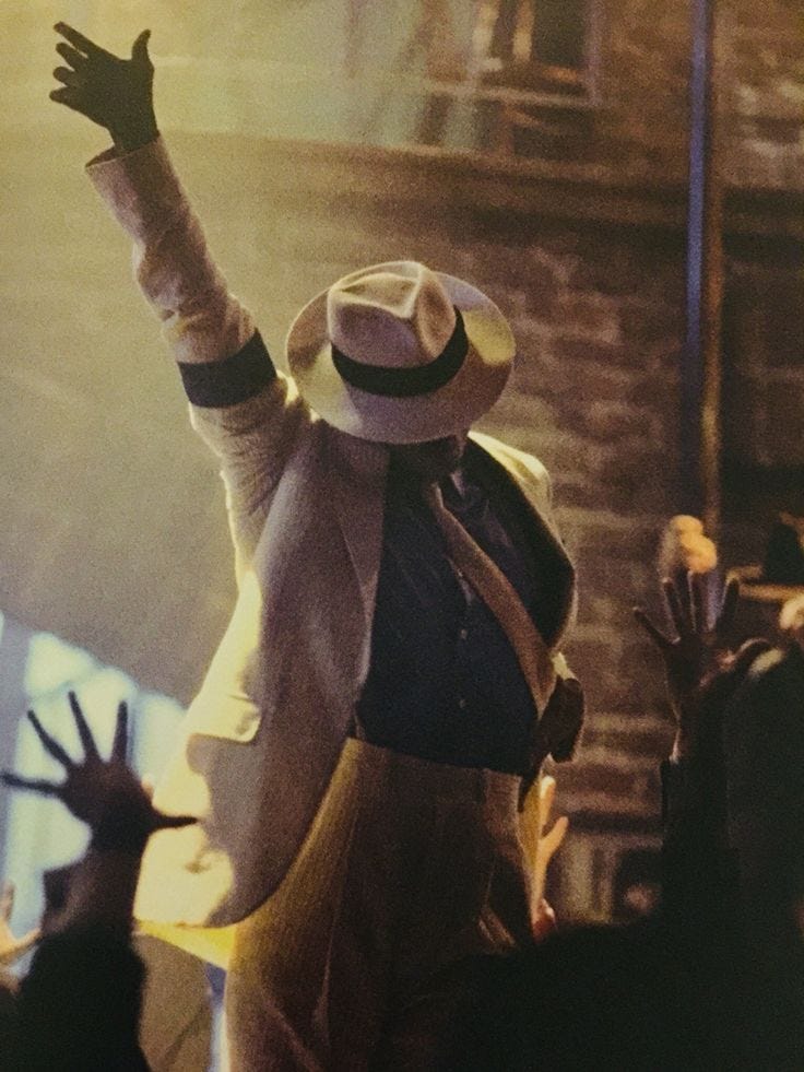 This may contain: a man with his arms up in the air at a concert wearing a hat and coat