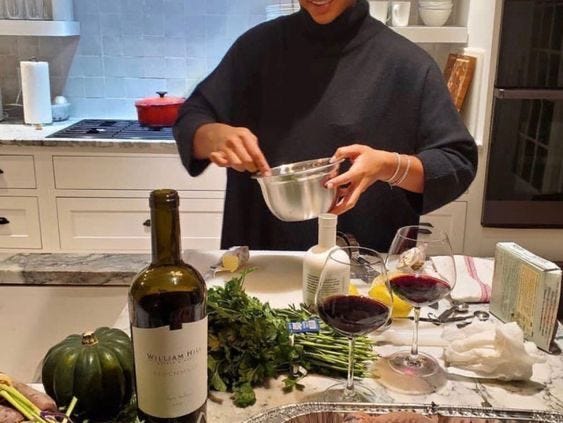 This may contain: a woman pouring wine into a bowl on top of a counter next to vegetables and fruit