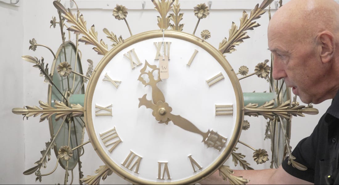 A gold and white clock with a man standing to the right of it A gold and white clock with a man standing to the right of it