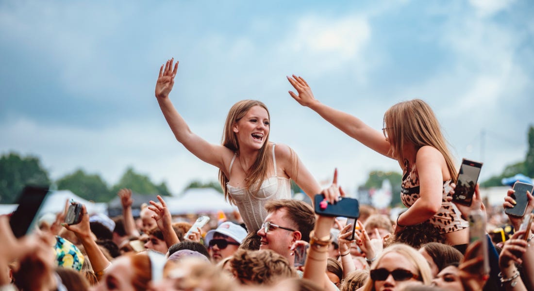 Two girls in a crowd at Splendour Festival on people's shoulders with their arms up
