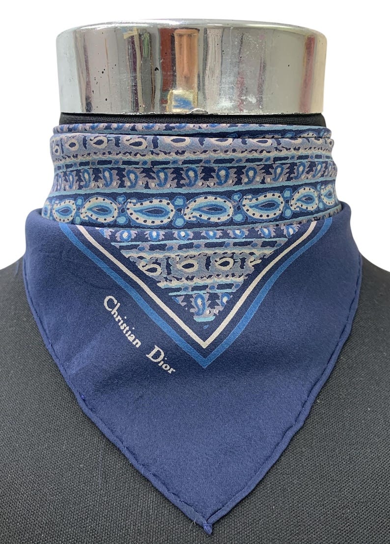 May include: A blue paisley patterned silk scarf with a white border and the words 'Christian Dior' in white text.