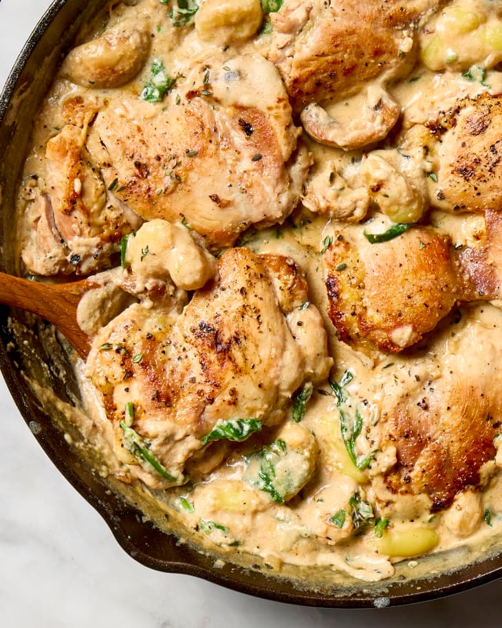 close up shot of one pan garlic parmesan chicken gnocchi in a cast iron skillet with a wooden spoon resting in the pan. close up shot of one pan garlic parmesan chicken gnocchi in a cast iron skillet with a wooden spoon resting in the pan.