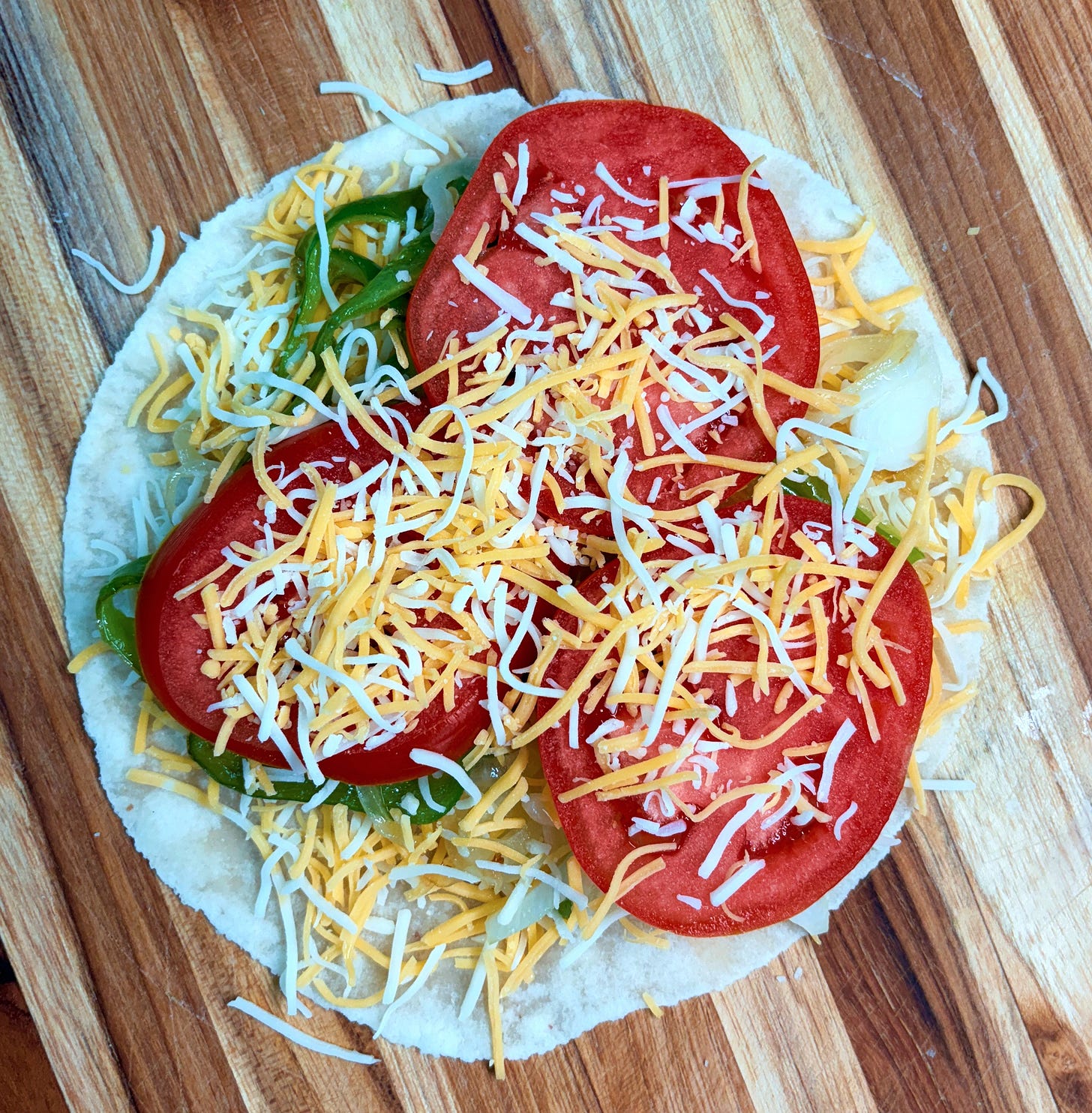 overhead view of a small tortilla with shredded cheese, peppers, onions, and tomatoes on it overhead view of a small tortilla with shredded cheese, peppers, onions, and tomatoes on it