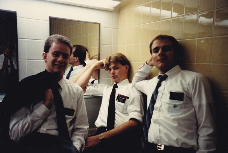 Three Mormon missionaries pose casually for the camera in a men's room tiled in yellow and white.
