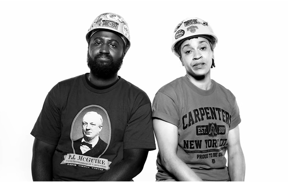 Video screenshot: Two African American carpenters, a bearded man and a woman, both wearing Carpenters Union T-shirts and hard hats Video screenshot: Two African American carpenters, a bearded man and a woman, both wearing Carpenters Union T-shirts and hard hats