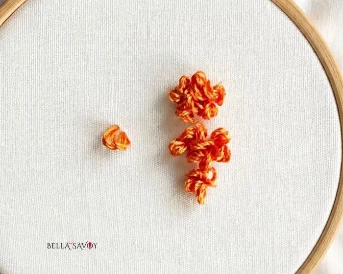 The Cross Stitch & Loop Stitch 62 loop stitch cluster on right, single loop stitch on left, in orange on hooped fabric