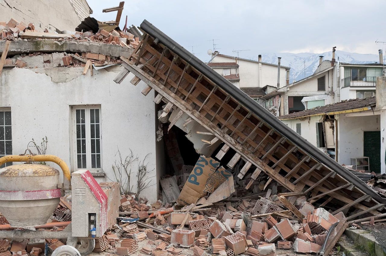 A photo of a house severely damaged by an earthquake. Part of the roof has collapsed and bricks are all over the ground from a damaged wall. A photo of a house severely damaged by an earthquake. Part of the roof has collapsed and bricks are all over the ground from a damaged wall.