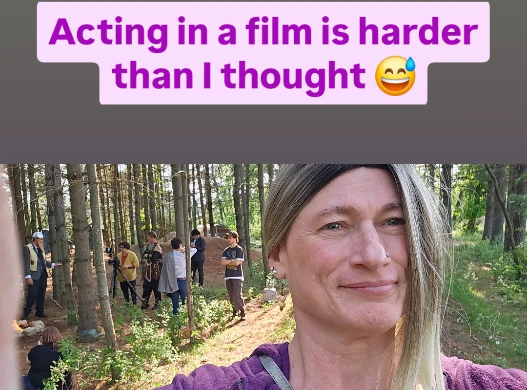 Selfie of Davi Gray, wearing a maroon sweatshirt and shoulder-length blond hair, in the woods. Over her shoulder, a film crew gathers around a camera on a tripod. Text in a bubble reads, "Acting in a film is harder than I thought 😅"