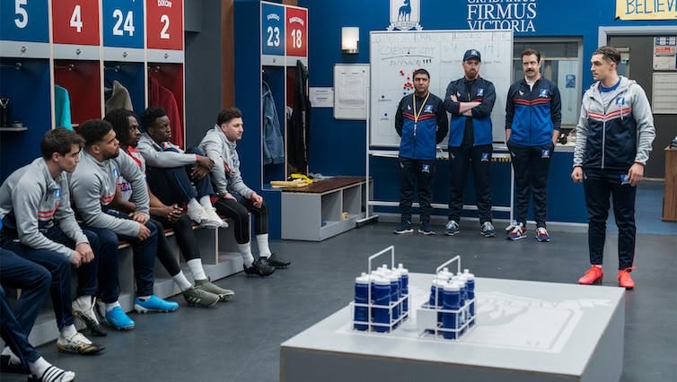 Ted Lasso and his AFC Richmond players in the dressing room. Ted and the other coaches stand in front of a whiteboard filled with tactics. Ted Lasso and his AFC Richmond players in the dressing room. Ted and the other coaches stand in front of a whiteboard filled with tactics.