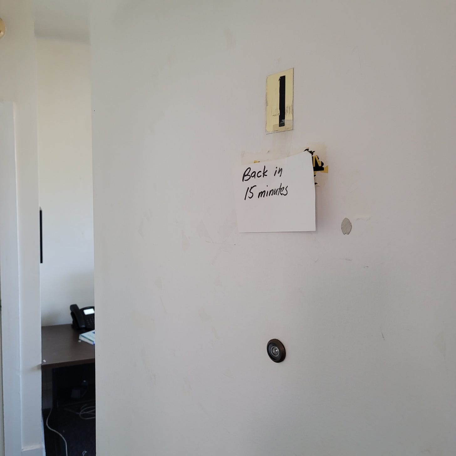 Index card taped to office door with "Back in 15 minutes" handwritten in black Sharpie.