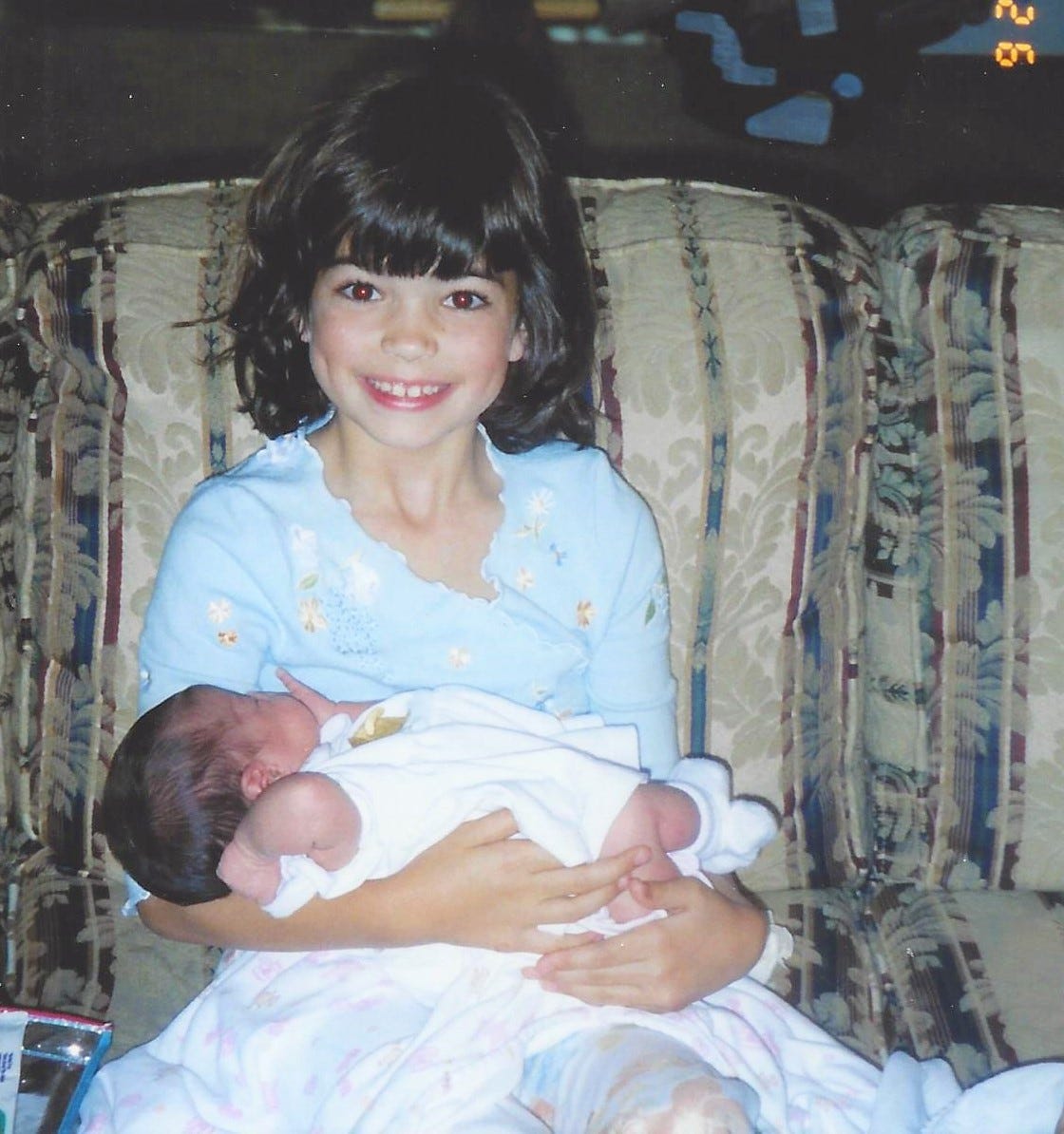 A 7-year-old girl cradling her new baby cousin on a sofa
