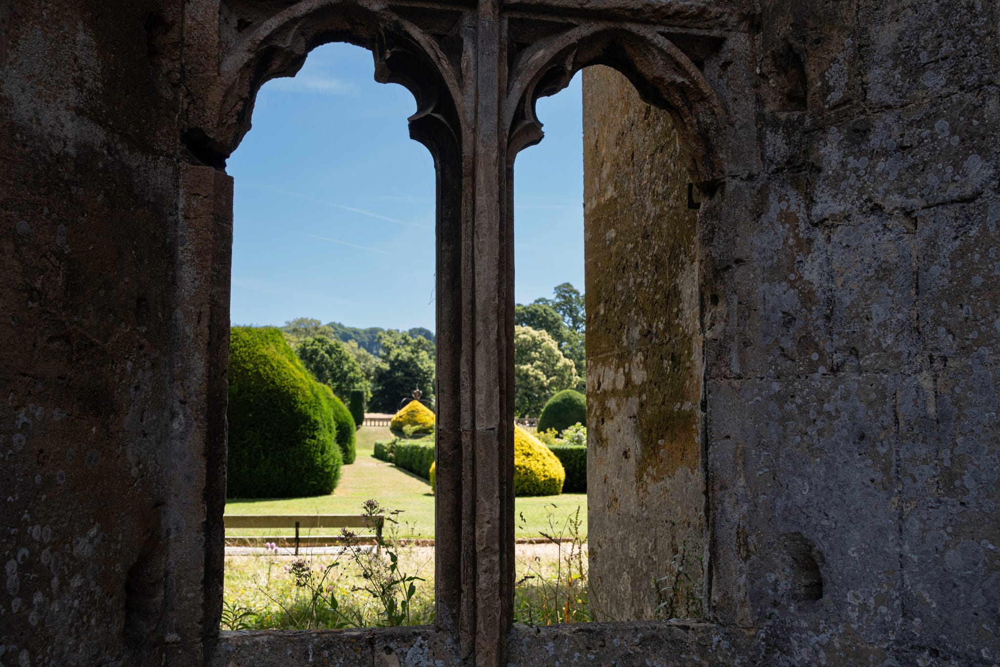 Window of ancient ruins looking out on a lanscape, manicured garden and a wooden bench