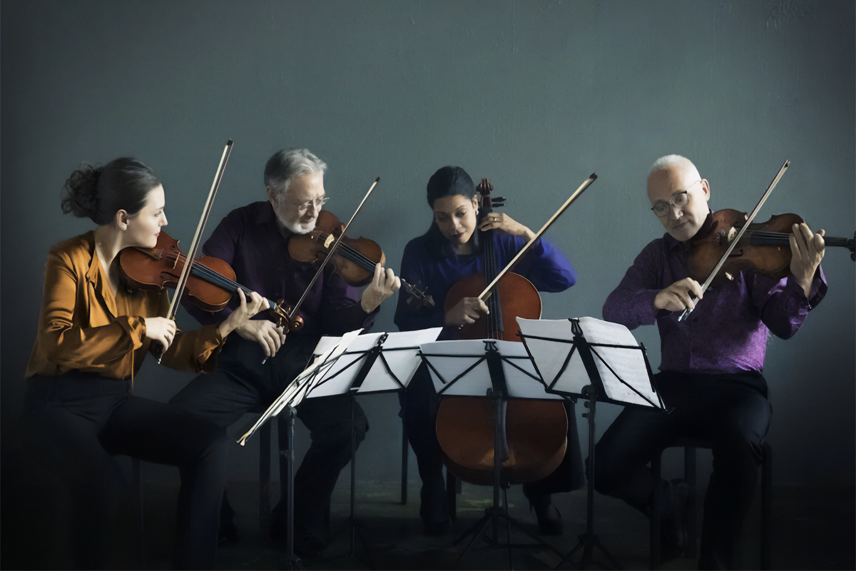 Four string musicians rehearse together, watching one another closely while reading from sheet music.