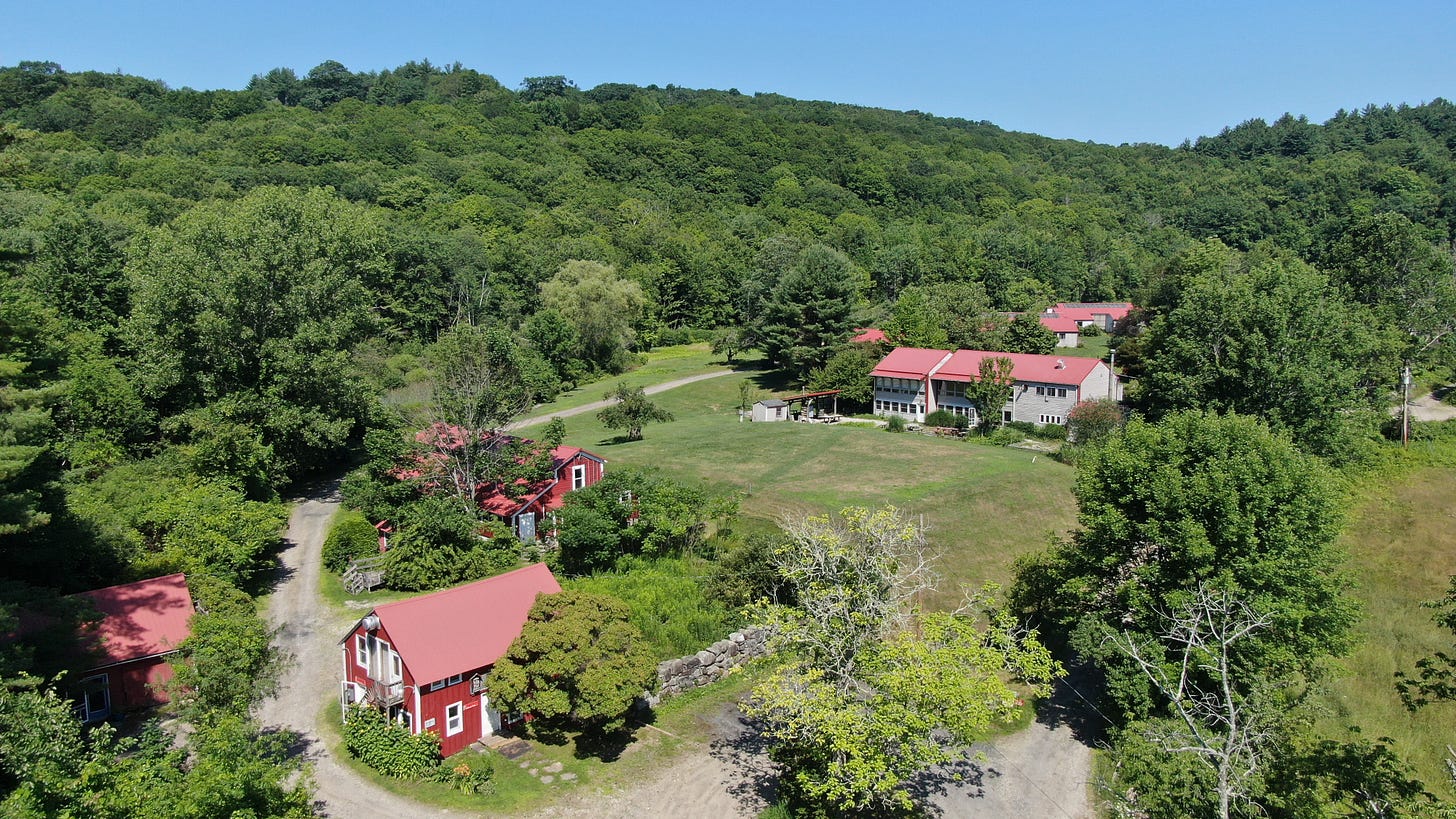 Aerial view of Snow Farm – the New England Craft Program – nestled in the lush foothills of Massachusetts' Berkshire Mountains, featuring red-roofed buildings surrounded by trees and open grassy areas. Aerial view of Snow Farm – the New England Craft Program – nestled in the lush foothills of Massachusetts' Berkshire Mountains, featuring red-roofed buildings surrounded by trees and open grassy areas.