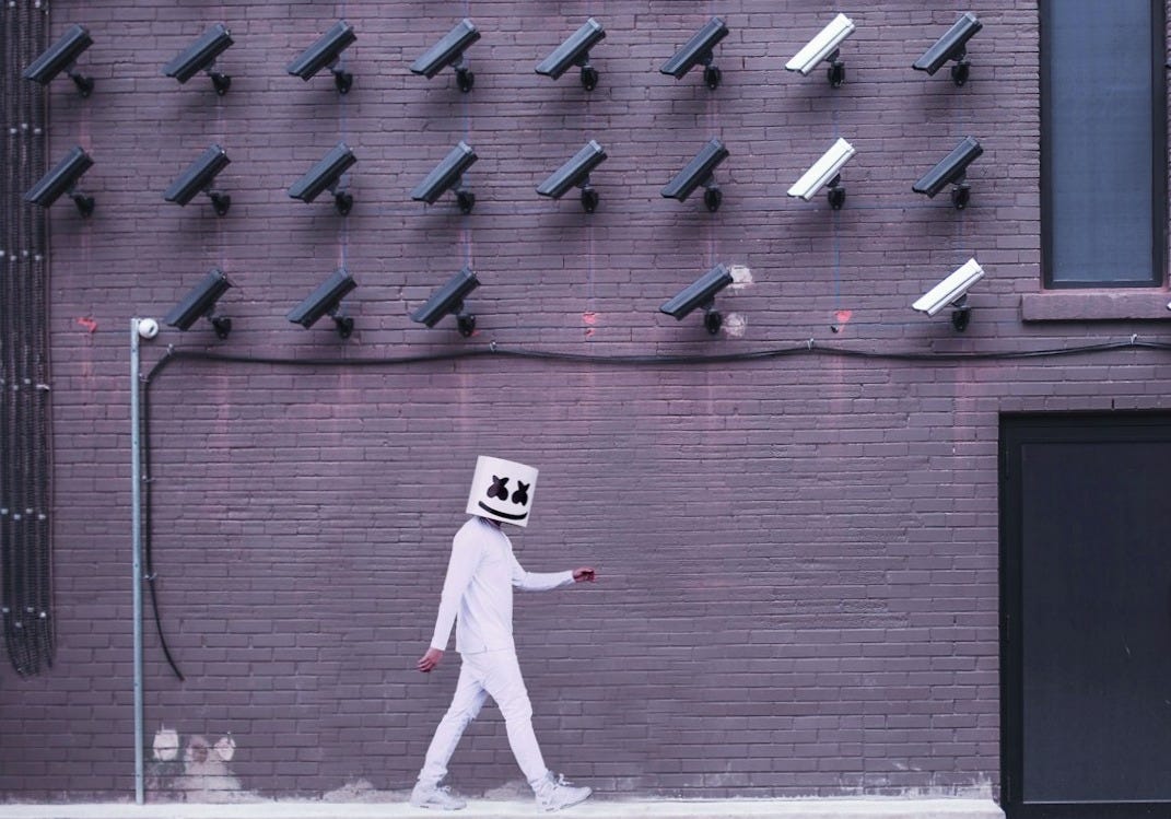 Marshmello walking down the side of the road with camera on the top of the building
