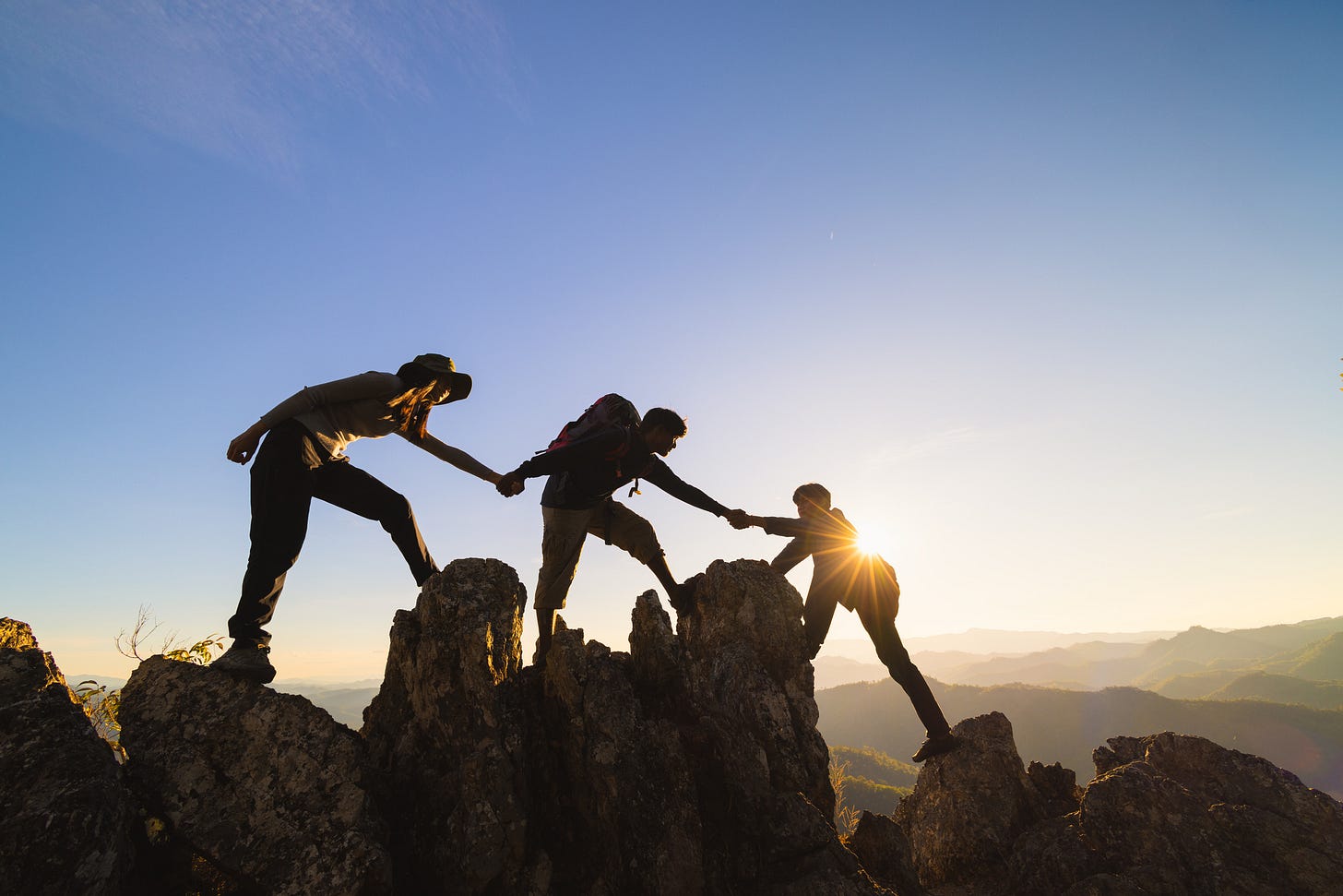 Friends helping each other climb a mountain.