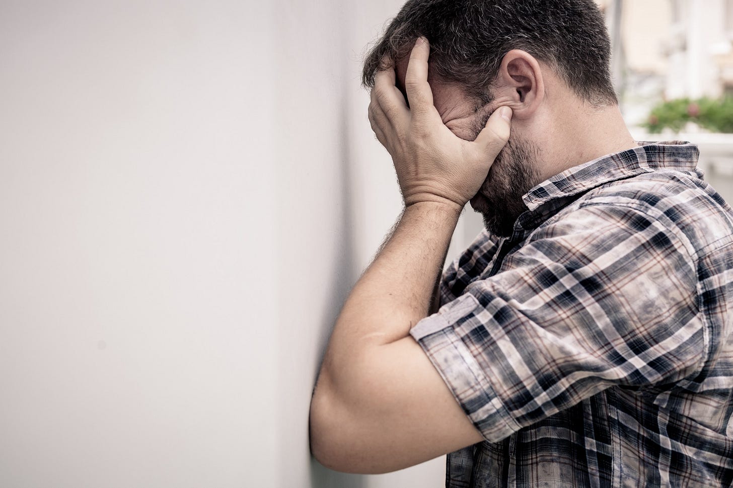 A frustrated man holds his head in his hands and leans against a wall.