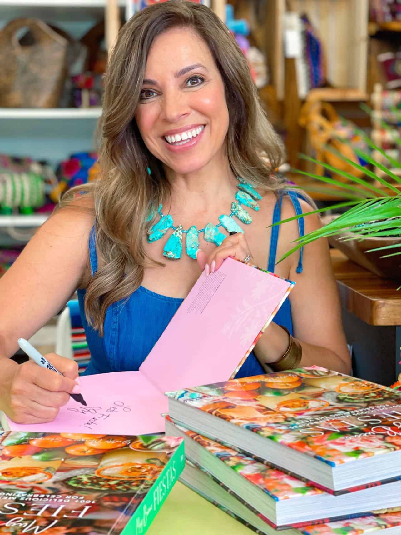 Yvette Marquez-Sharpnack signing copies of her cookbook Muy Bueno Fiestas at a book event, wearing a turquoise necklace and blue dress. Yvette Marquez-Sharpnack signing copies of her cookbook Muy Bueno Fiestas at a book event, wearing a turquoise necklace and blue dress.