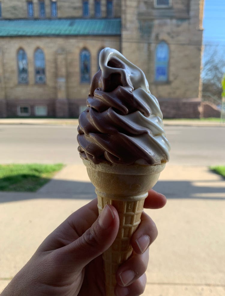 a photo of a chocolate and vanilla swirl ice cream cone held in a hand. In the background is a sidewalk and a church. a photo of a chocolate and vanilla swirl ice cream cone held in a hand. In the background is a sidewalk and a church.