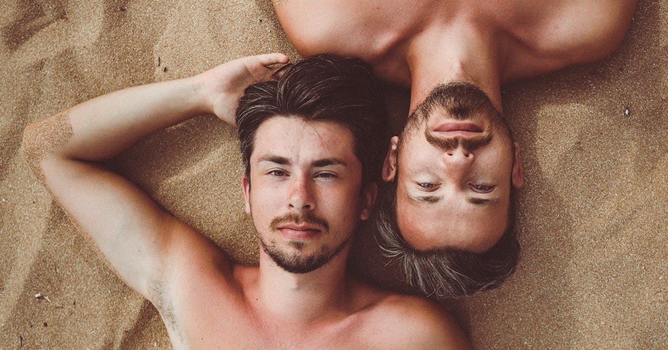 topless man lying on brown sand during daytime