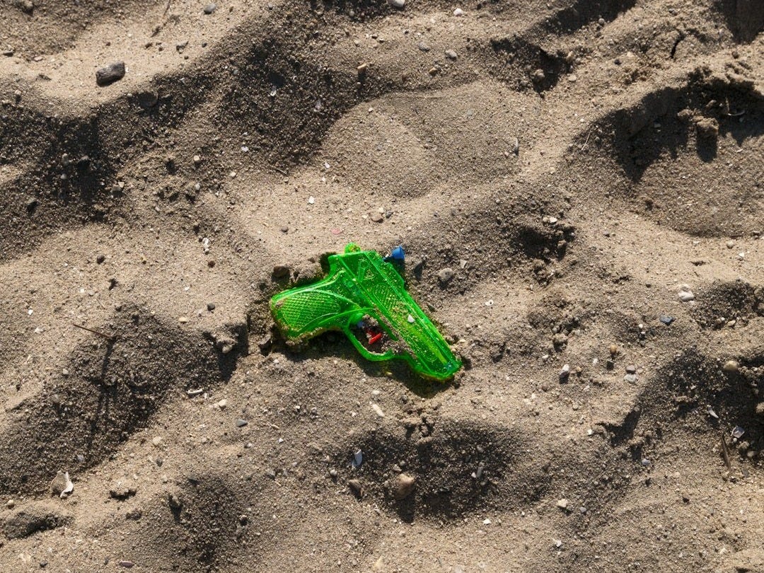 A green water gun rests on the sandy beach.