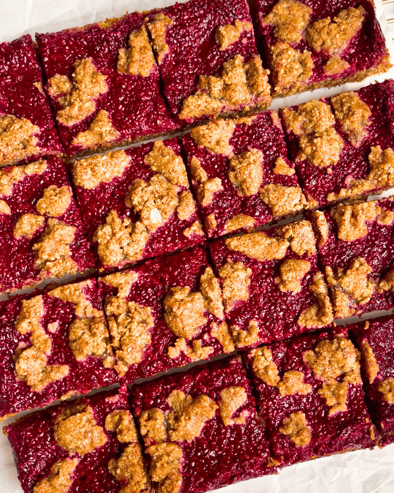 raspberry jam oat bars on a white parchment paper, sliced into squares