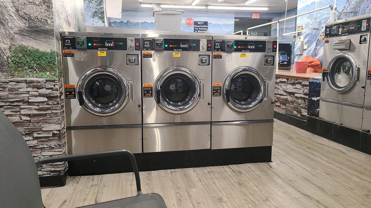 Row of commercial washers with commercial dryers in the background