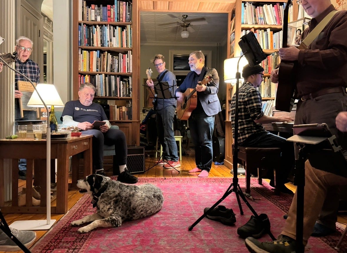 a group of white musicians play piano, washboard, guitar, in a living room lined with bookcases. a dog lies on a pink carpet. a group of white musicians play piano, washboard, guitar, in a living room lined with bookcases. a dog lies on a pink carpet.