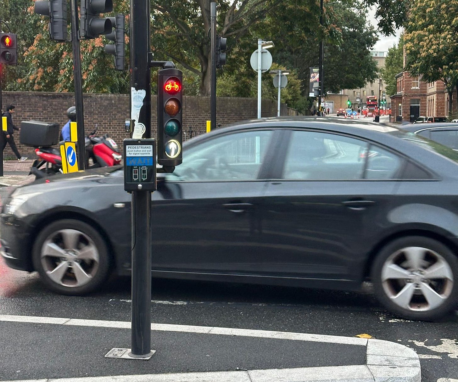 A junction with traffic lights for cyclists, next to a standard pedestrian 'wait' button.