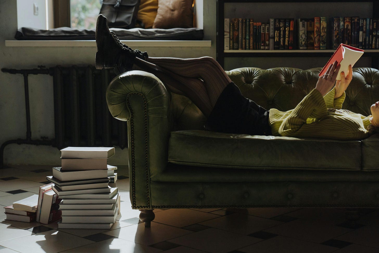 girl wearing a green sweater lying on a leather couch reading a book with a red cover girl wearing a green sweater lying on a leather couch reading a book with a red cover