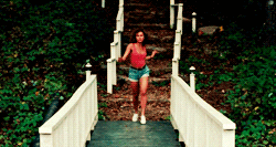 A retro movie clip of Jennifer Grey as Baby in Dirty Dancing, balancing and dancing joyfully on a wooden garden bridge outdoors surrounded by green trees.