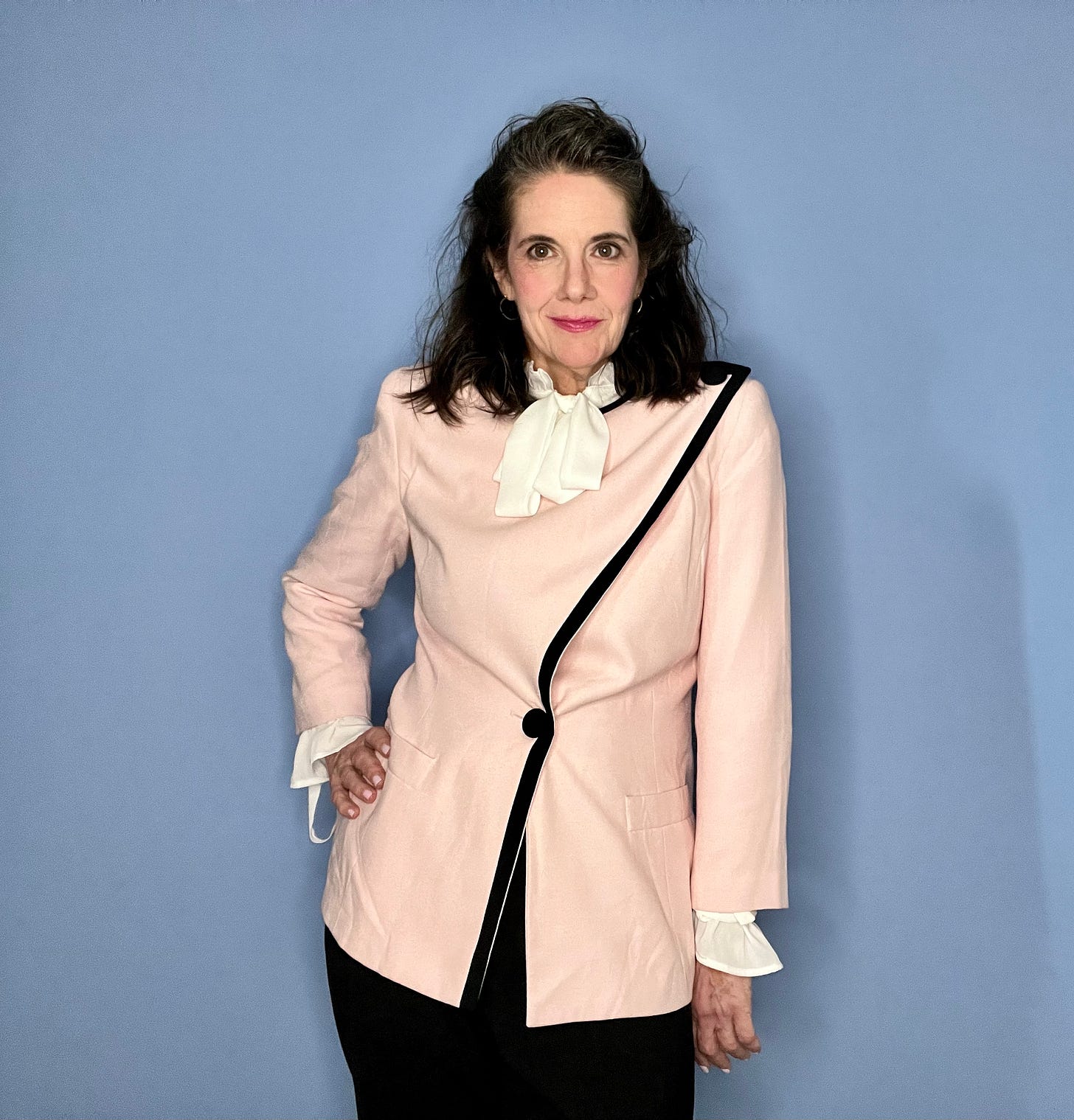 Woman in 1980's style hair, and clothes, a pink blazer and black pants