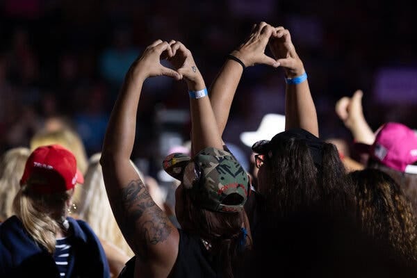 A pair of Trump supporters hold their hands over their heads to form hearts amid a crowd of his supporters at a rally. 