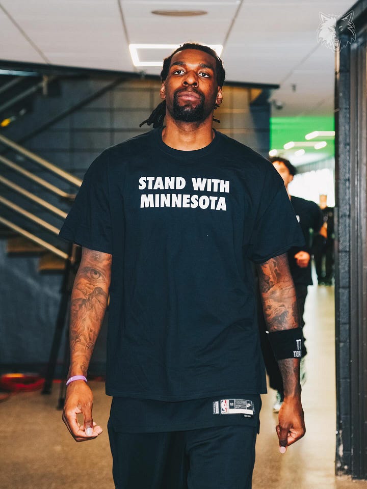 Very tall basketball players wearing black t-shirts that say Stand With Minnesota in white block letters