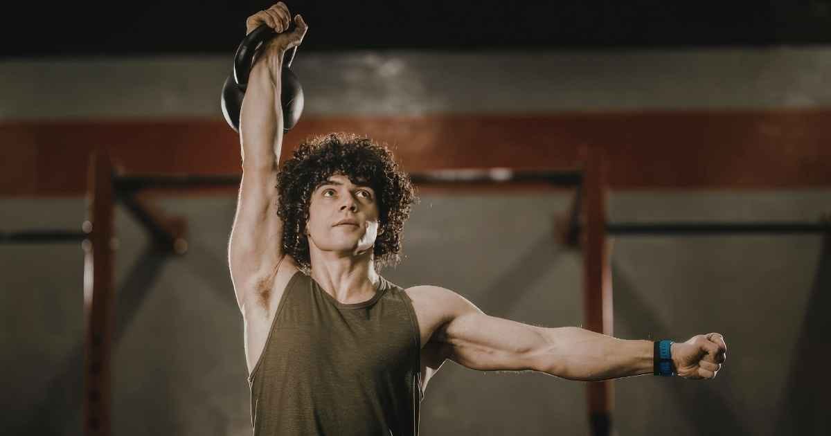 Man performing kettlebell overhead press exercise in gym setting Man performing kettlebell overhead press exercise in gym setting