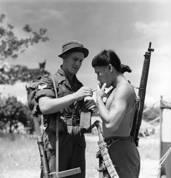 A British soldier shares a cigarette with an Iban Tracker in Sarawak, Borneo, 1950, highlighting an unlikely alliance.
