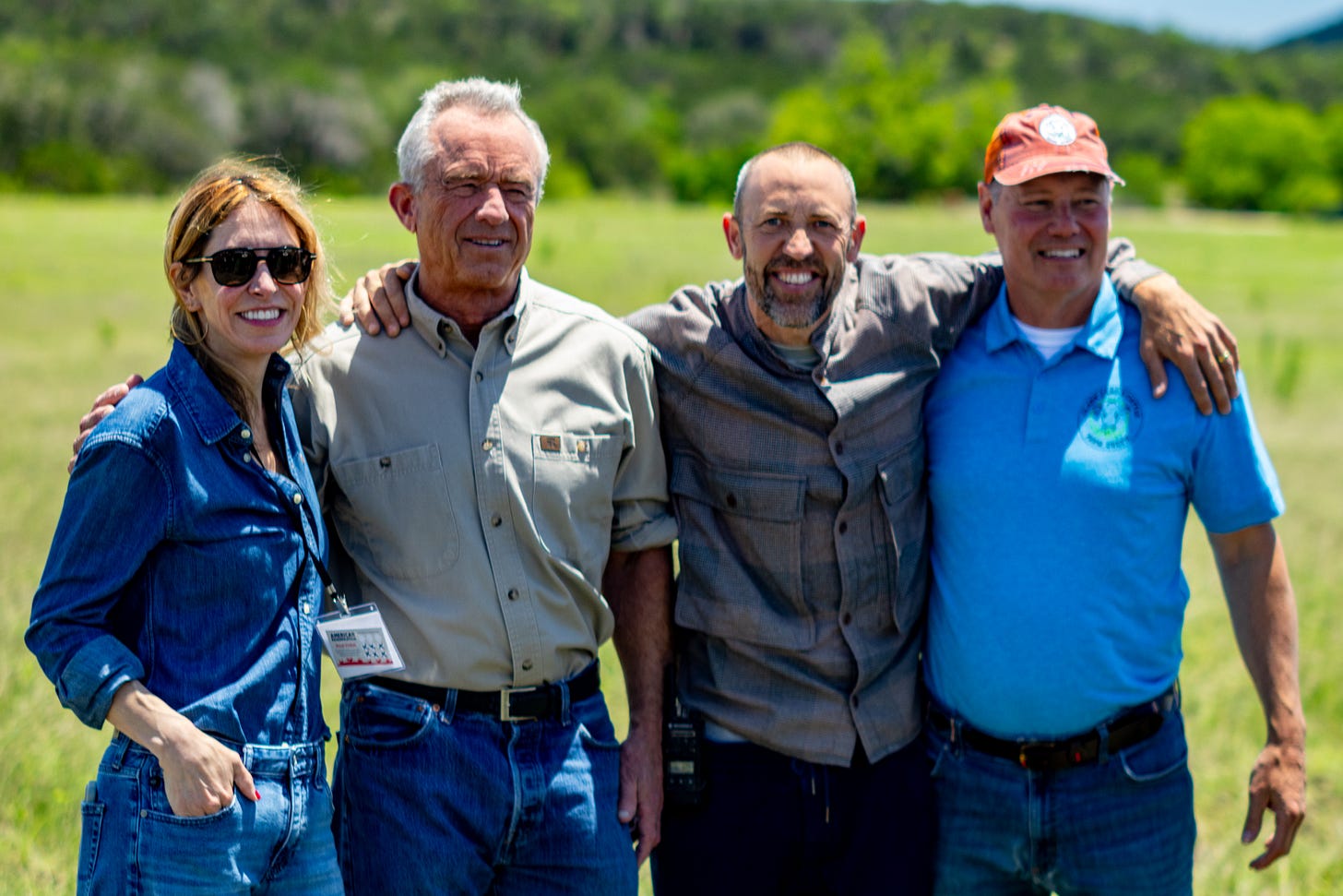 Four people stand arm-in-arm in a Texas field, including HHS Secretary Robert F. Kennedy Jr., smiling at the camera.