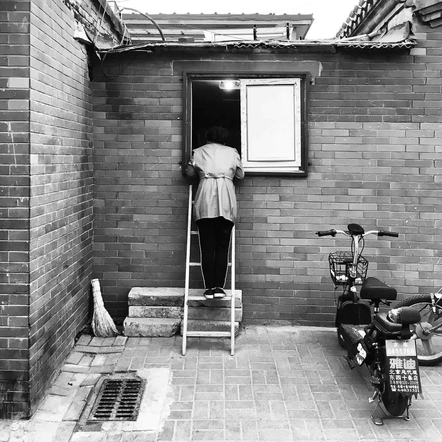 Customer on a ladder at the window of a bricked-up shop in one of Beijing’s ancient hutongs Customer on a ladder at the window of a bricked-up shop in one of Beijing’s ancient hutongs