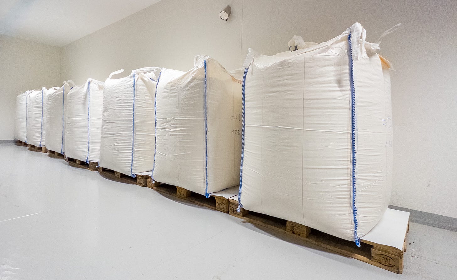 Im hellen Lagerraum einer Industrie-Mühle stehen sechs grosse weisse Big Bags mit Mehl dicht nebeneinander auf Paletten. Die Säcke sind hoch aufgerichtet und oben zusammengebunden. Im hellen Lagerraum einer Industrie-Mühle stehen sechs grosse weisse Big Bags mit Mehl dicht nebeneinander auf Paletten. Die Säcke sind hoch aufgerichtet und oben zusammengebunden.