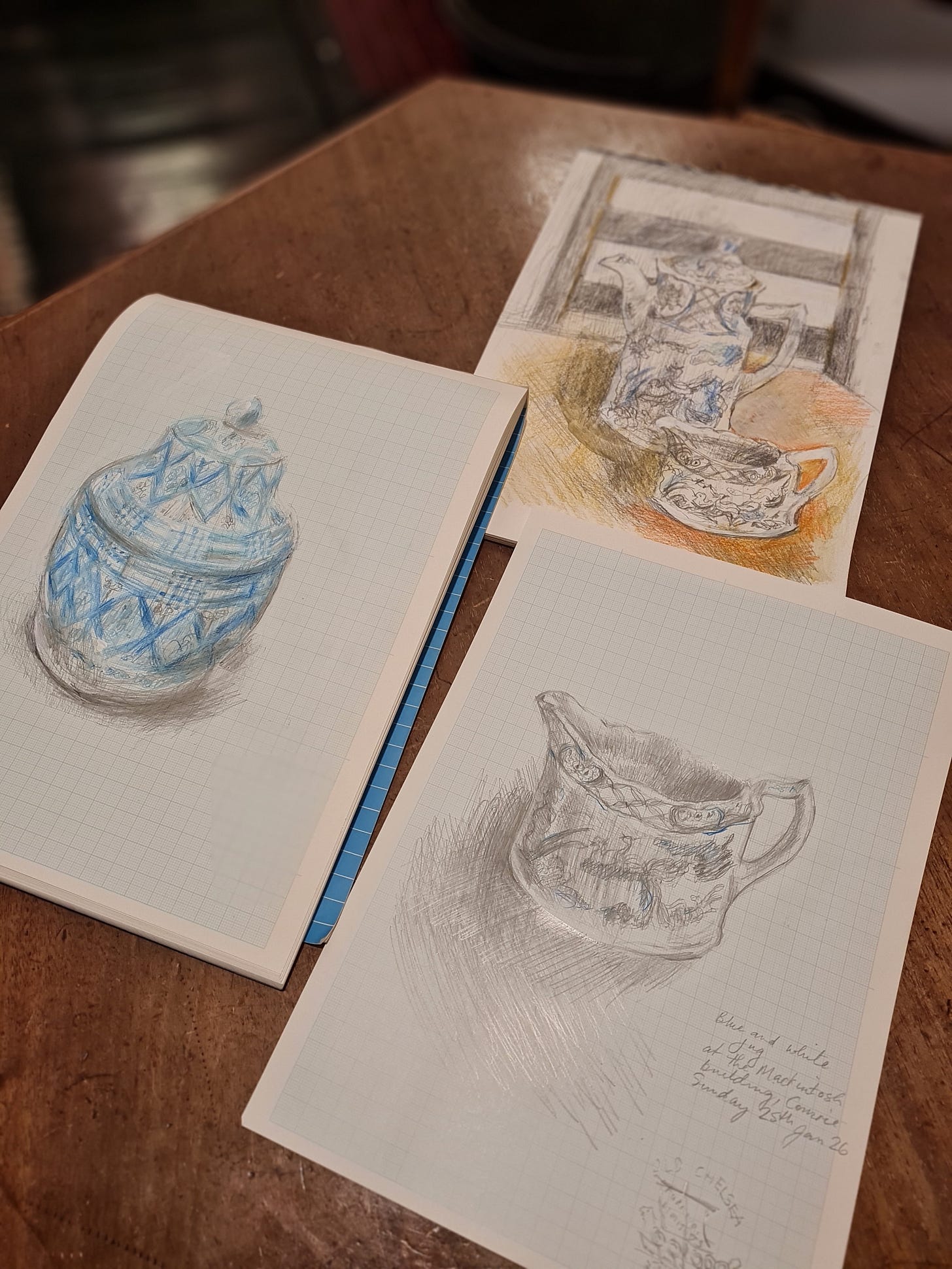 Three drawings of crockery are lying on a wooden table.
