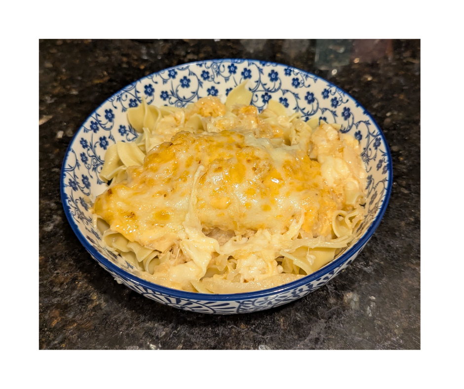 A blue and white bowl filled with egg noodles and topped with chicken and broiled cheese.