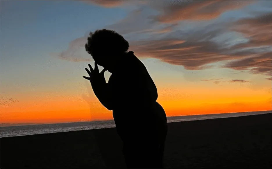 silhouette of a praying woman with the sunset and ocean in the background