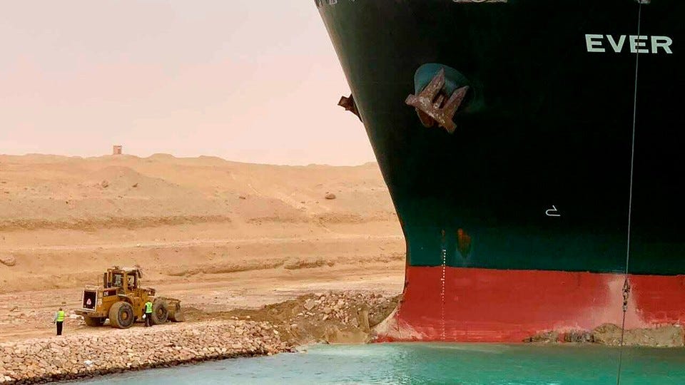 Cargo ship stranded in desert sand with construction equipment nearby.