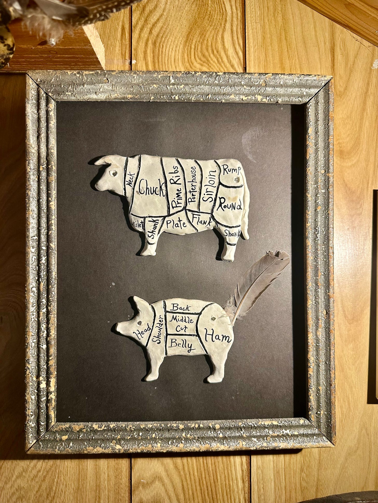 framed clay sculptures of a cow and pig with butchering charts on their backs