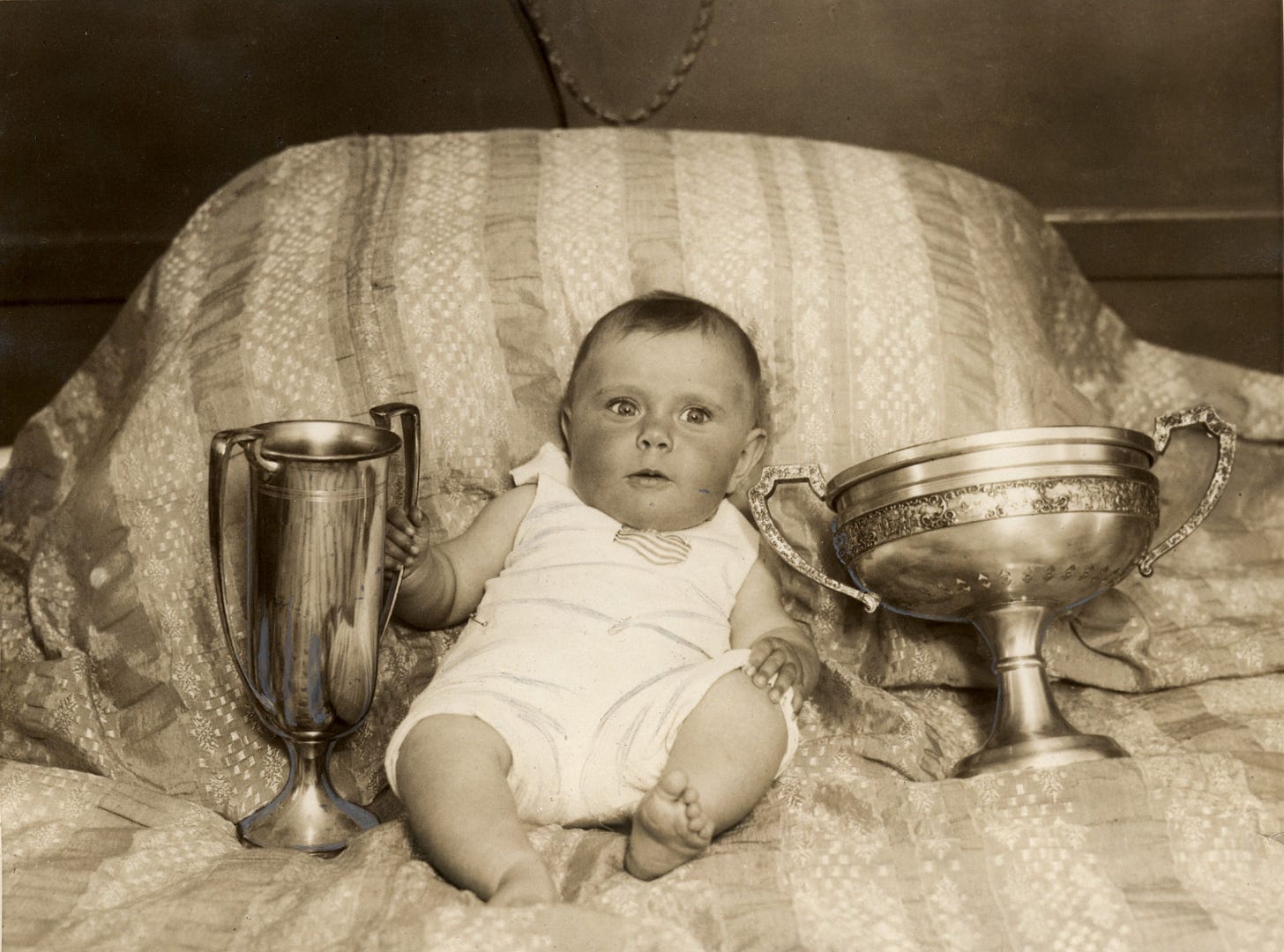 A baby with two huge trophies. He looks very confused about what's happening.