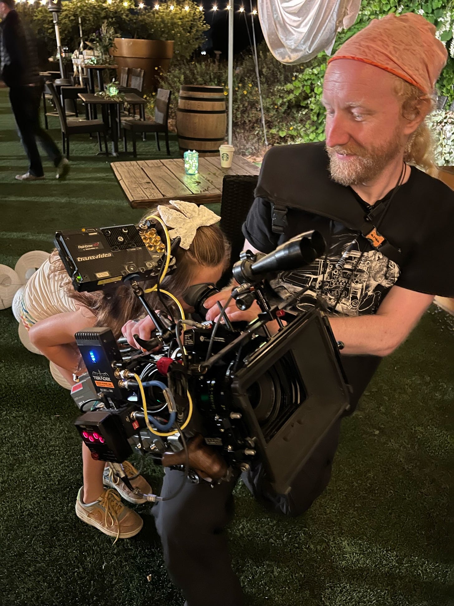Cinematographer David Auner gives the flower girl a look through a camera on a busy wedding reception set.